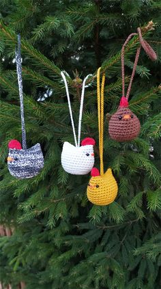 three crocheted ornaments hanging from a pine tree in the shape of chickens and roosters