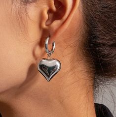 Add a touch of romance to your look with our Silver Heart Earrings. These trendy hoop earrings feature delicate, dangling silver heart pendants that add a touch of chic romance to your jewelry collection. Top to Bottom Length: 4cm Heart Pendant Width: 2cm Material: Stainless Steel Earring posts are made from high quality surgical grade stainless steel Earrings are 100% nickel-free and cadmium-free Earrings are hypoallergenic and tarnish resistant Trendy Hoop Earrings With Heart Charm, Trendy Pierced Heart Earrings, Valentine's Day Minimalist Hoop Earrings, Pierced Hoop Earrings For Valentine's Day, Trendy Silver Hoop Earrings With Heart Charm, Trendy Silver Single Heart Earring, Valentine's Day Heart Detail Earrings, Silver Heart Earrings With Dangling Charms, Trendy Heart-shaped Nickel-free Hoop Earrings