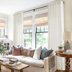 a living room filled with lots of furniture next to a window covered in white curtains