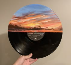 a hand holding up a record with a painting on it's side, in front of a wall