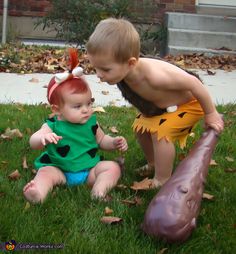 two young children are playing in the grass with fake dinosaurs on their heads and tails