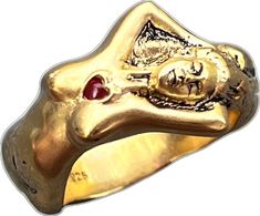 a gold ring with a red stone in the center and a face on it's side