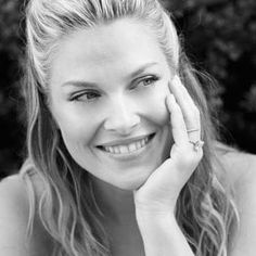 black and white photograph of a smiling woman with her hand on her face, looking at the camera