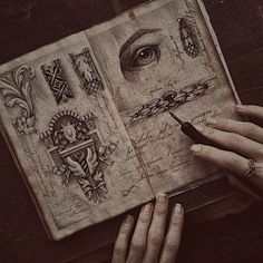 a woman's hands holding an open book with drawings on it and writing in the pages