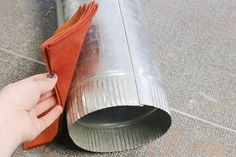 a hand is holding an orange cloth near a metal pipe on the ground with it's end sticking out