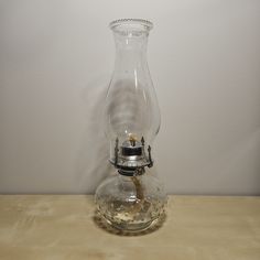 a clear glass vase with a silver lid on a wooden table next to a white wall