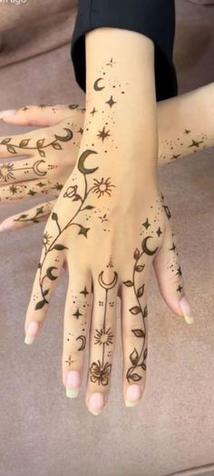 a woman's hand with tattoos on it and stars and moon designs painted on her hands