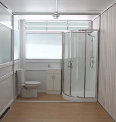 a bathroom with a toilet, shower and sink in it's corner stall next to a window