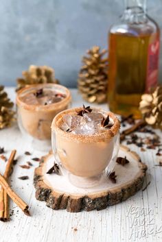 two glasses filled with hot chocolate and cinnamon sitting on top of a wooden table next to pine cones