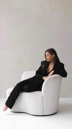 a woman sitting in a white chair with her legs crossed on the armrests