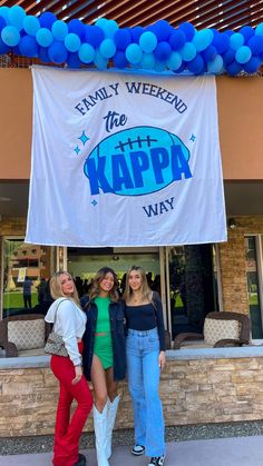 three women standing in front of a building with a banner hanging from the ceiling above them