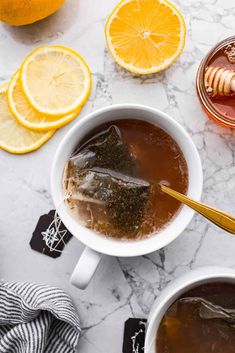 two mugs filled with tea, lemon slices and honey on a marble counter top