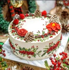 a decorated cake sitting on top of a table next to pine cones and red berries