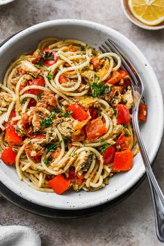 a white bowl filled with pasta, tomatoes and parsley on top of a table