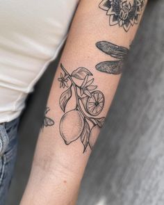 a woman's arm with tattoos on it and an olive branch, lemons and leaves