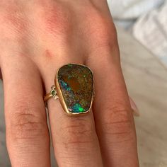 a woman's hand wearing a gold ring with an opal stone in it