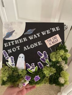 someone holding up a graduation cap decorated with fake flowers and grass that reads, either way we're not alone the end is near