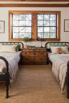 two twin beds in a room with wooden floors and large windows, one has a dog laying on the bed