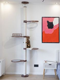 a cat tree in the corner of a room next to a painting on the wall