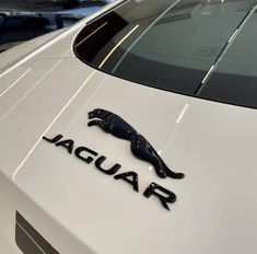 the front end of a white car with a black jaguar logo on it's hood