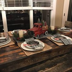 a table set for christmas with plates and place settings on it in front of a window