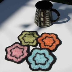 four flower rugs sitting on top of a table next to a coffee mug and spoon