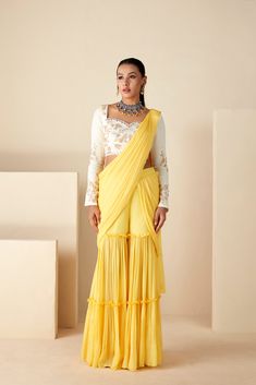 This ensemble boasts a pre-draped sharara saree in vibrant yellow and white hues, exuding elegance with every fold. Paired with a beautifully handcrafted blouse, featuring a sweetheart neckline and full sleeves, this ensemble epitomizes timeless grace. Crafted from luxurious georgette crepe, both the saree and blouse are meticulously designed for comfort and style. Elevate your ethnic wardrobe with this exquisite ensemble, perfect for special occasions and celebrations. Designer Pre-draped Yellow Saree, Elegant Yellow Palazzo Set With Traditional Drape, Yellow Designer Wear Pre-draped Saree, Yellow Pre-draped Designer Saree, Yellow Palazzo Set With Dupatta For Reception, Yellow Palazzo Set For Reception And Navratri, Elegant Yellow Pre-draped Saree With Traditional Drape, Yellow Palazzo Set For Diwali Reception, Yellow Palazzo Set For Reception Diwali