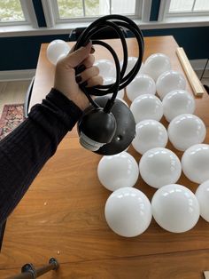 a person is holding a light bulb over some white balls on a wooden table with windows in the background