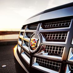 the front grille of a black and silver car with its lights on at sunset or sunrise