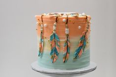 a multicolored cake decorated with feathers and beads on a silver stand against a white background