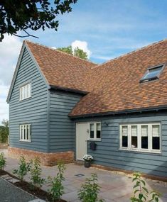 a blue house with brown shingles on the roof and brick walkway leading up to it