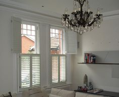 a living room filled with furniture and a chandelier hanging from the ceiling next to two windows