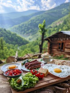 a wooden table topped with plates of food next to a forest filled mountain side covered in trees