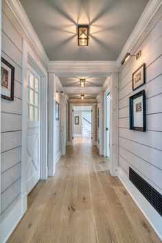 an empty hallway with white walls and wood floors, framed pictures on the wall and wooden flooring