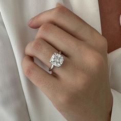 a woman's hand with a diamond ring on her left hand, wearing a white shirt