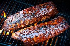 two steaks cooking on the grill with flames