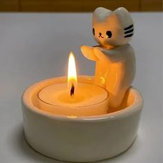 a white cat candle holder with a lit candle in it