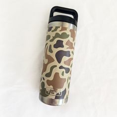 thermos cup is sitting on top of a white sheet with a camouflage pattern