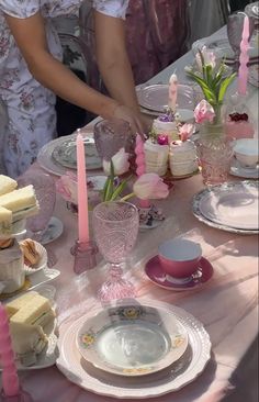 the table is set with pink and white dishes, plates, cups, and candles