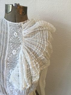 "Vintage Victorian white cotton net and lace blouse with long sleeves and a very large flouncy ruffle coming off a crochet placard down the front. The net has pintuck creating a ribbon effect The sleeves each have two functioning buttons and a small trim of lace. The waist is gathered to create a ruffle around and is backed with ribbon. The whole blouse is lined with net. The blouse buttons down the back with a covered placard to hide the buttons. Single hook and eye at waist. Simple crew neck. Lace Top With Ruffles For Daywear, White Lace Top With Ruffles, White Victorian Style Top With Lace Work, Victorian Ruffle Blouse For Daywear, White Lace Collar Top For Daywear, Daywear Victorian Lace Dress With Ruffles, Daywear Lace Victorian Dress With Ruffles, Lace Victorian Dress With Ruffles For Daywear, Fitted Cotton Lace Top With Ruffles