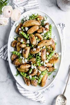 a white plate topped with chicken and green beans covered in feta cheese next to a spoon