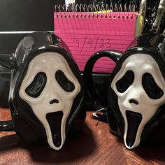 two black and white mugs with faces on them sitting on a desk next to a notepad