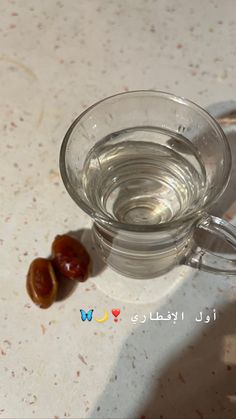 a glass cup filled with water sitting on top of a white counter next to a piece of fruit