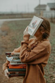 a woman holding a stack of books in front of her face and covering her eyes