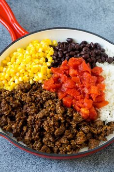 mexican food in a skillet with corn, black beans, rice and chili on the side