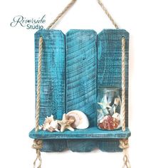 a blue shelf with seashells on it and rope hanging from the bottom, in front of a white wall