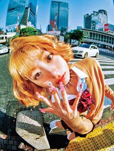 a woman with red hair is posing on a bench in the city while holding her hand up to her mouth