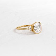 a yellow gold ring with an oval cut diamond in the center and two small diamonds on each side