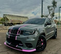 a grey jeep with pink stripes parked in a parking lot next to a train track