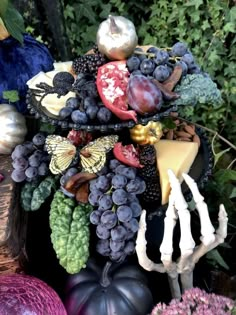 an arrangement of fruit and vegetables is displayed in front of some plants, including grapes